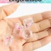 Hand holding clear resin beads with pink rose patterns.