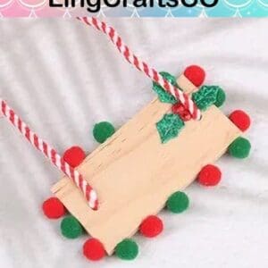 Wooden sled ornament with red and green pom-poms, holly leaves, and striped cord.