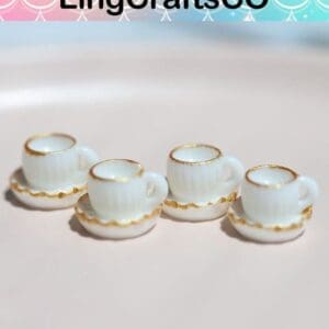 Four miniature white teacups with gold trim on saucers, displayed on a pastel background.