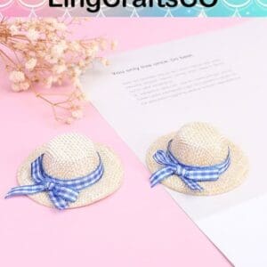 Two mini straw hats with blue ribbons on a pink surface next to dried flowers and a paper.