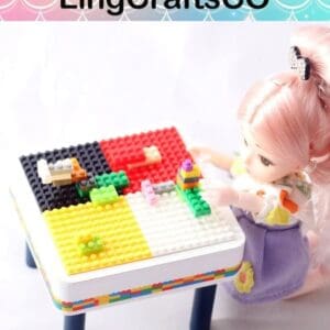 A doll with pink hair sits at a colorful building blocks table, assembling small structures.