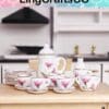 Miniature tea set with pink floral design on a wooden table, kitchen background.