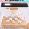 Miniature tea set with floral patterns on a small wooden table in front of a dollhouse kitchen.
