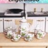 Miniature floral tea set on a wooden surface with cups, saucers, teapot, and plates. Kitchen background.