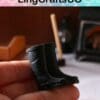 Hand holding miniature black rubber boots, with a stove and broom in the blurred background.