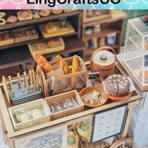 Miniature bakery display with baguettes, a cake, utensils, and a jar of biscuits on a wooden cart.