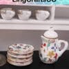 Miniature floral ceramic tea set with cups, plates, and a teapot, displayed on a shelf.