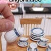 Person holding a miniature teapot over a wooden table with stacked plates and cups, featuring blue patterns.