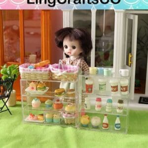 Doll behind a mini bakery display with pastries and drinks on a grass-like surface, showcasing LingCraftsCO products.