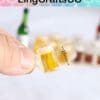 Hand holding a tiny 15mm beer mug with a blurred background of bottles and mugs.