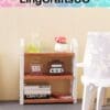 Miniature shelf with books, bottles, a vintage radio, and a flower pot, beside a patterned chair.