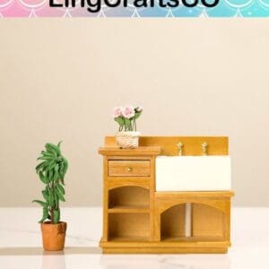 Miniature wooden sink with faucet, potted plant, and pink flowers on counter, set against a neutral background.