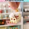 Hand holding a miniature shopping basket with two tiny drink containers, shelves with miniature products in background.