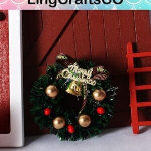 Miniature Christmas wreath with gold baubles, red berries, and a "Merry Christmas" sign, displayed against a wooden backdrop.