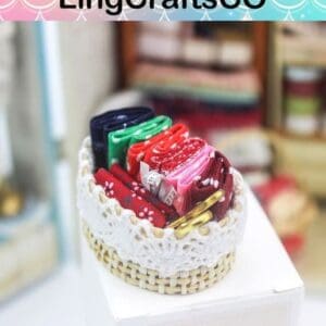Miniature basket with colorful folded fabrics, topped with a crochet lace trim. Background shows blurred crafts.