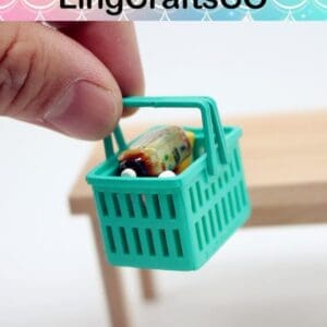 Fingers holding a miniature shopping basket with groceries inside, positioned above a wooden table.