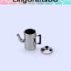 Miniature silver teapot with a lid placed beside it on a light blue background.