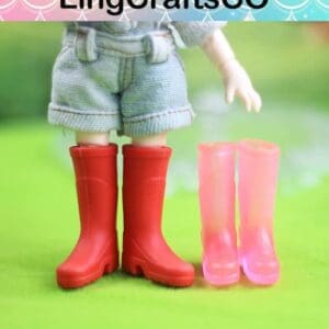 Doll wearing red boots with denim shorts next to a pair of translucent pink boots on green surface.