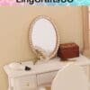 Miniature vanity set with oval mirror, perfume bottle, wooden box, and a small white brush on a white table.