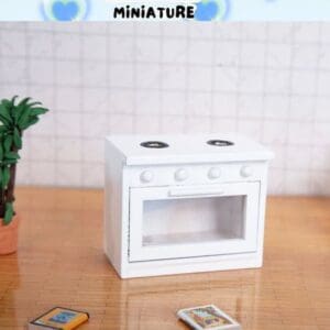 Miniature white stove with two burners on a wooden surface, next to a small plant and two tiny books.