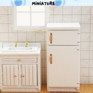 Miniature white kitchen set with a sink, cabinet, and fridge against a tiled wall.